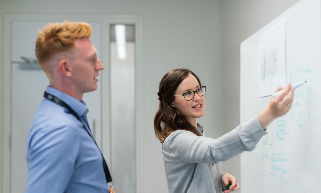 Två personer diskuterar och skriver på whiteboard under möte